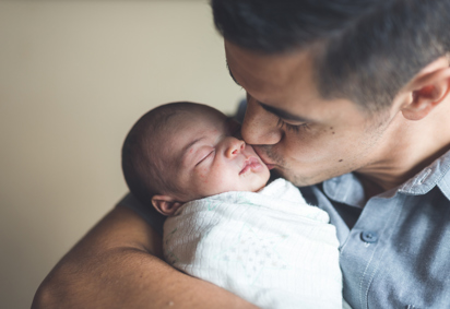 An ethnic dad gently kisses his newborn daughter on the cheek