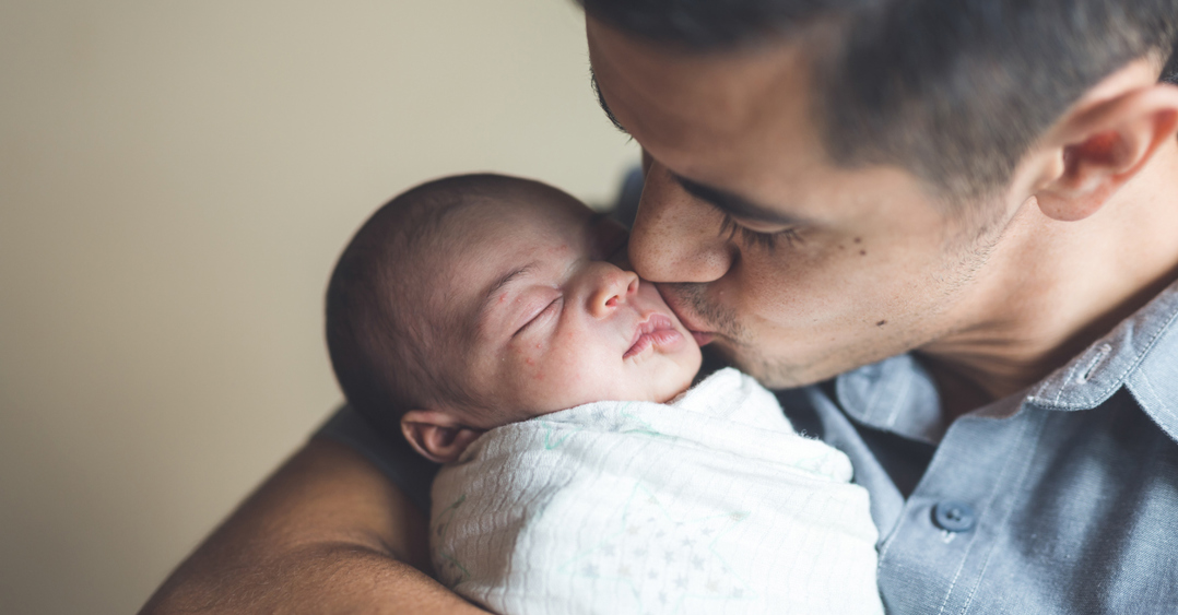 An ethnic dad gently kisses his newborn daughter on the cheek
